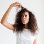 Girl with curly hair touching her hair with an unhappy expression, showing the need for hair masks best for curly hair.