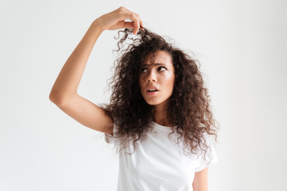 Girl with curly hair touching her hair with an unhappy expression, showing the need for hair masks best for curly hair.