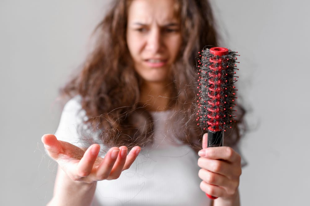 Worried woman holding a hairbrush in one hand and fallen hair in the other hand, concerned about hair fall and thin hair.